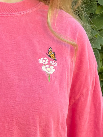 This pigment dyed T-shirt has a beautiful embroidered Monarch butterfly fluttering over the top of a white and pink Cosmo flower. Left chest embroidered graphic, 100% heavy cotton, garment dyed with a faded look and relaxed fit, available in watermelon pink. Size 5XL is a purple/rose pink color. Sizes S, M, L, XL, 2XL, 3XL, 4XL, and 5XL available.