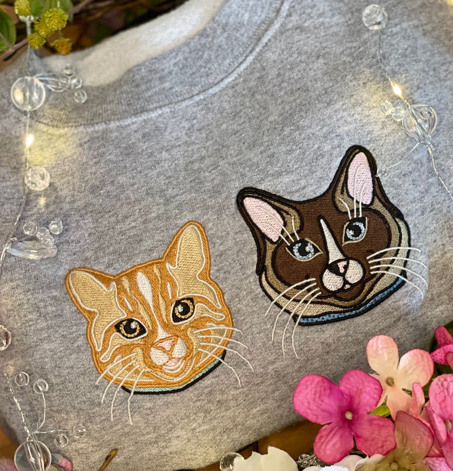 Ragdoll, Snowshoe, Siamese Cat embroidered on a crewneck sweatshirt design is 4x4 inches on the left chest. Available in sizes S-3XL and colors pigment pink, baby blue, and forest green. Shown on a grey sweatshirt surrounded by flowers. 