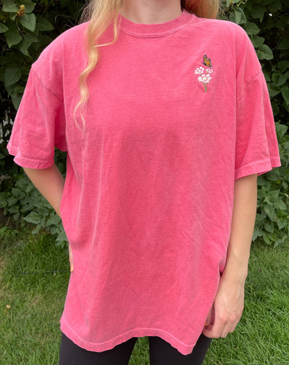 This pigment dyed T-shirt has a beautiful embroidered Monarch butterfly fluttering over the top of a white and pink Cosmo flower. Left chest embroidered graphic, 100% heavy cotton, garment dyed with a faded look and relaxed fit, available in watermelon pink. Size 5XL is a purple/rose pink color. Sizes S, M, L, XL, 2XL, 3XL, 4XL, and 5XL available.