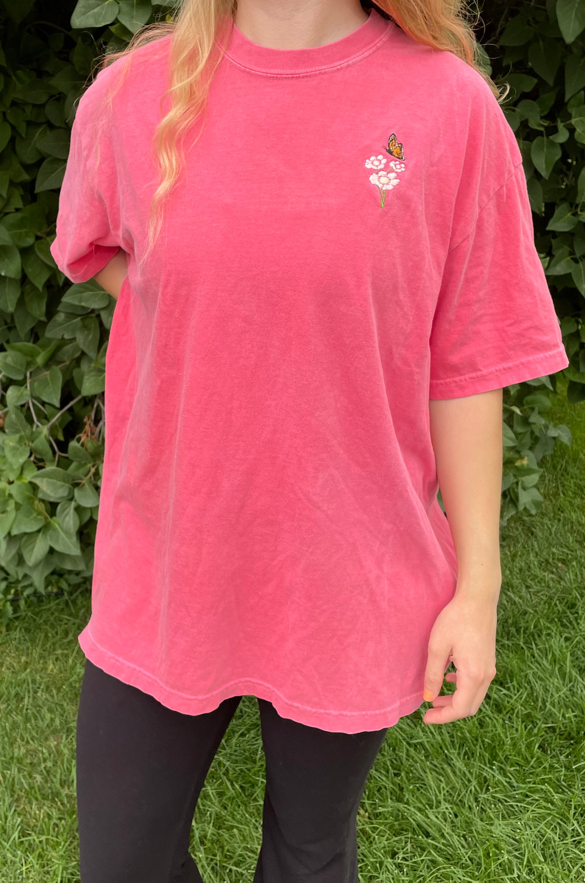 This pigment dyed T-shirt has a beautiful embroidered Monarch butterfly fluttering over the top of a white and pink Cosmo flower. Left chest embroidered graphic, 100% heavy cotton, garment dyed with a faded look and relaxed fit, available in watermelon pink. Size 5XL is a purple/rose pink color. Sizes S, M, L, XL, 2XL, 3XL, 4XL, and 5XL available.