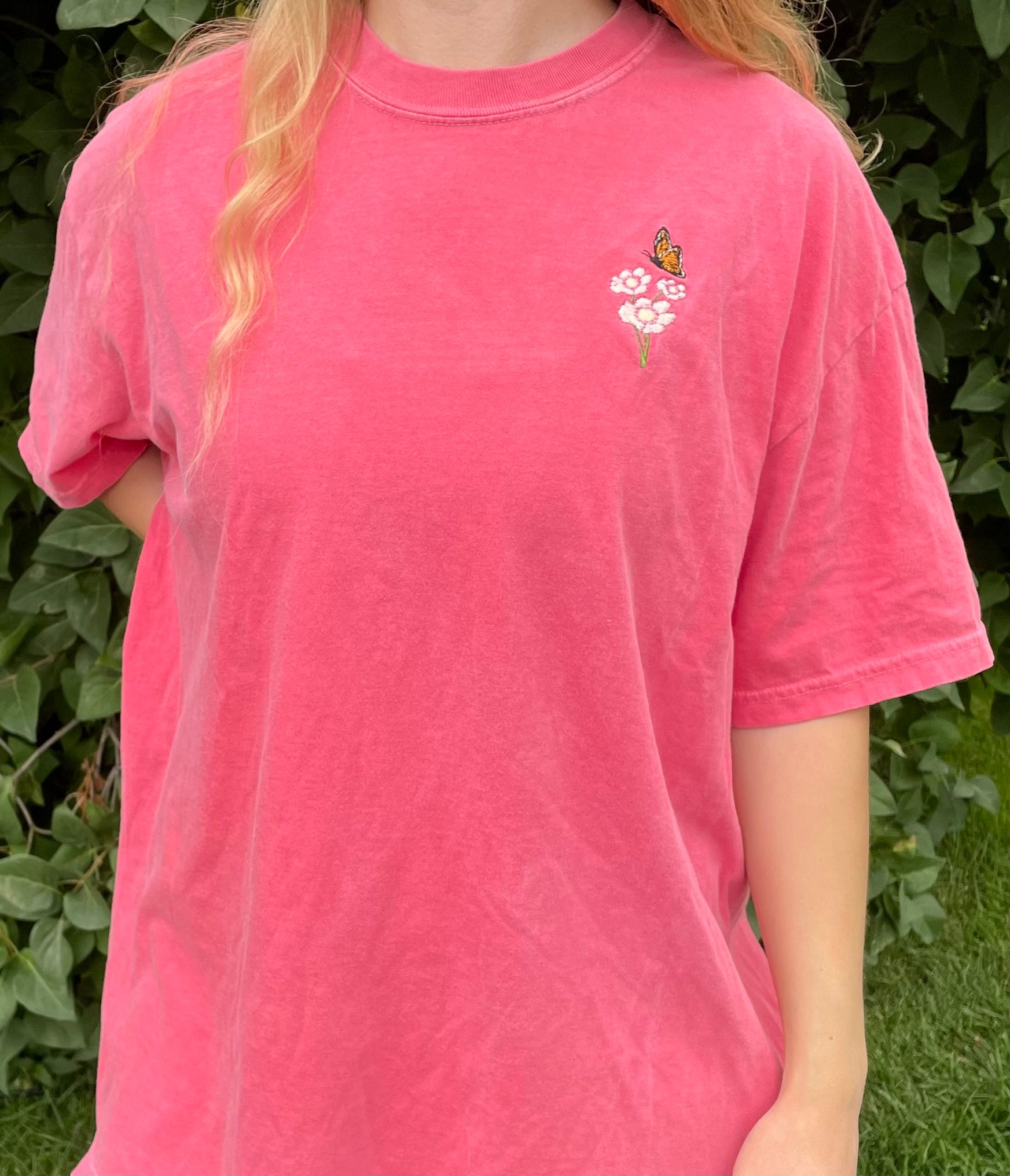 This pigment dyed T-shirt has a beautiful embroidered Monarch butterfly fluttering over the top of a white and pink Cosmo flower. Left chest embroidered graphic, 100% heavy cotton, garment dyed with a faded look and relaxed fit, available in watermelon pink. Size 5XL is a purple/rose pink color. Sizes S, M, L, XL, 2XL, 3XL, 4XL, and 5XL available.