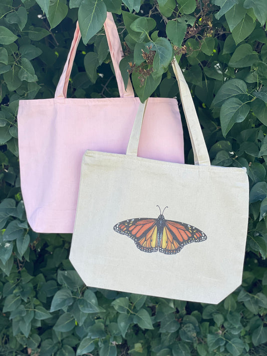 Front center of zippered tote bag large sparkle glitter Monarch butterfly with rich colors. Small version of sparkle Monarch butterfly on inside zippered pouch. Available in a light pink canvas tote or a natural tote color. 