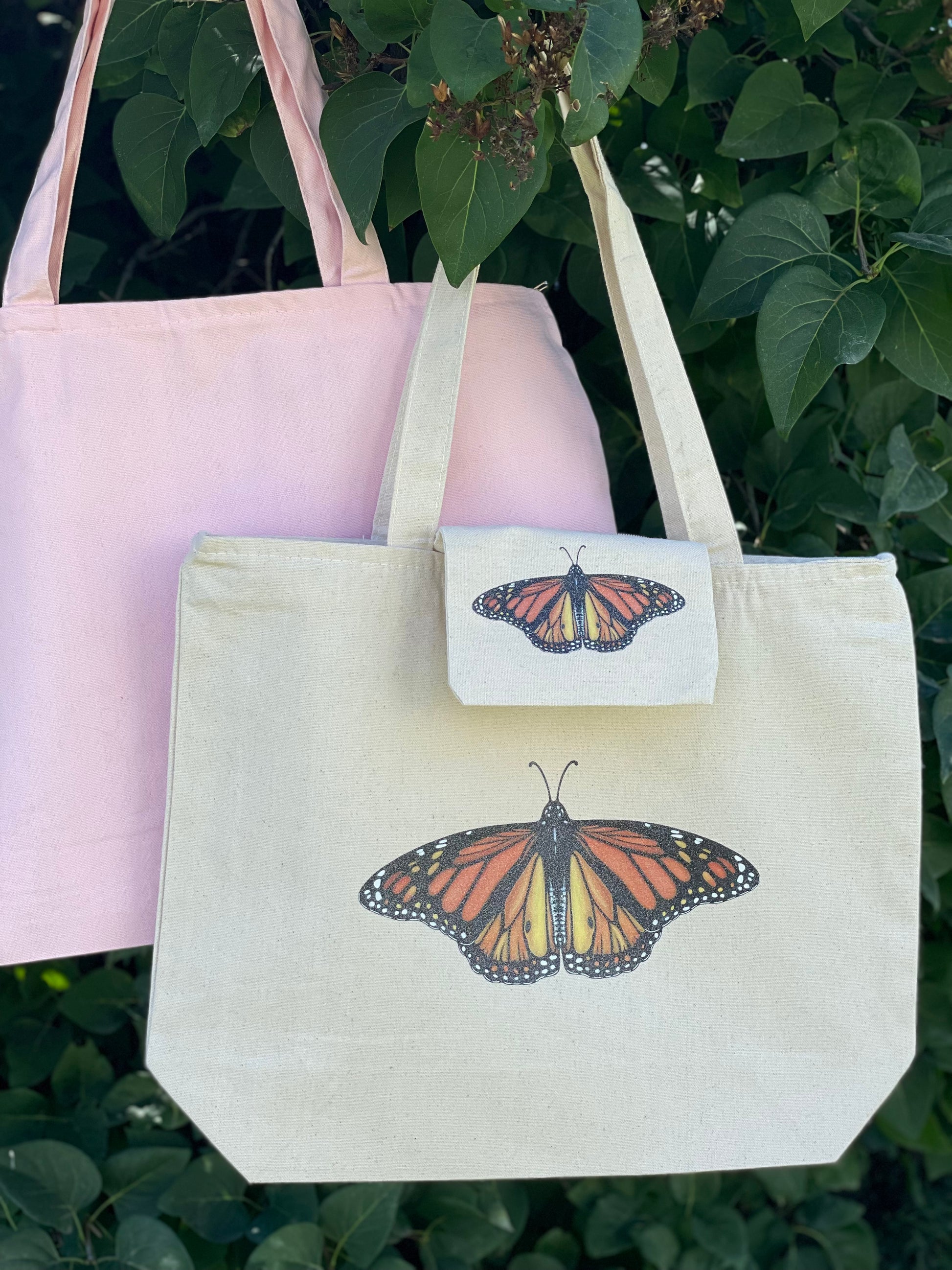 Front center of zippered tote bag large sparkle glitter Monarch butterfly with rich colors. Small version of sparkle Monarch butterfly on inside zippered pouch. Available in a light pink canvas tote or a natural tote color. 